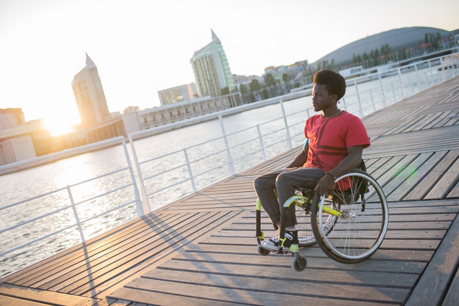 A man in a wheelchair rolling along a wide, level waterfront boardwalk at sunset