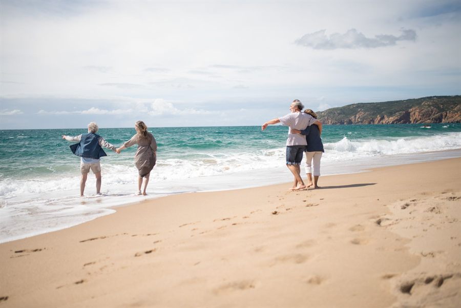 Older couple wading at the water’s edge on a sunny beach