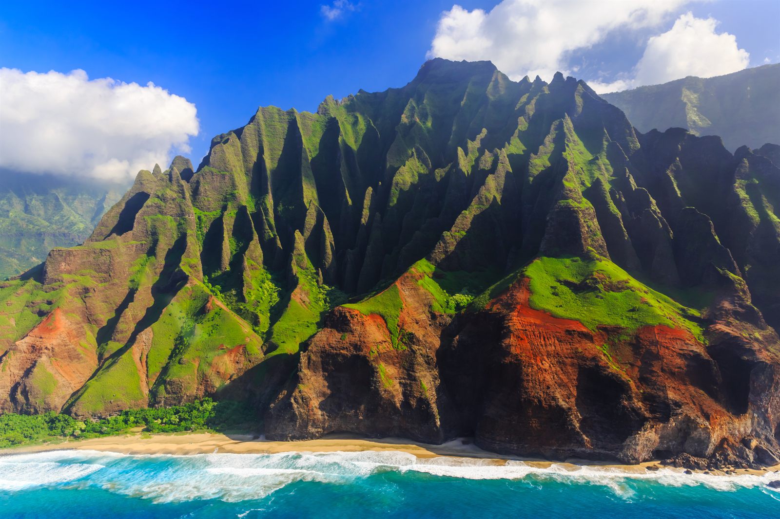 Green fluted cliffs of the Na Pali Coast on Kauai rising above blue water, seen from the air